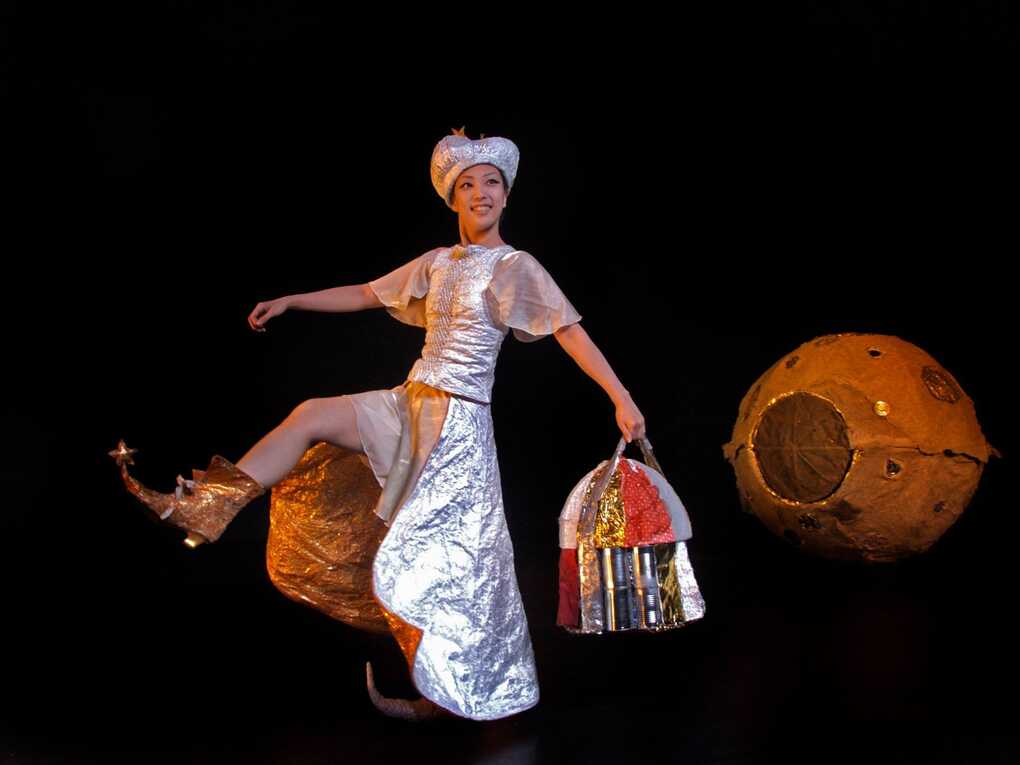 Moon Maiden stepping on a dark backgrounded stage, with the moon behind her on the right