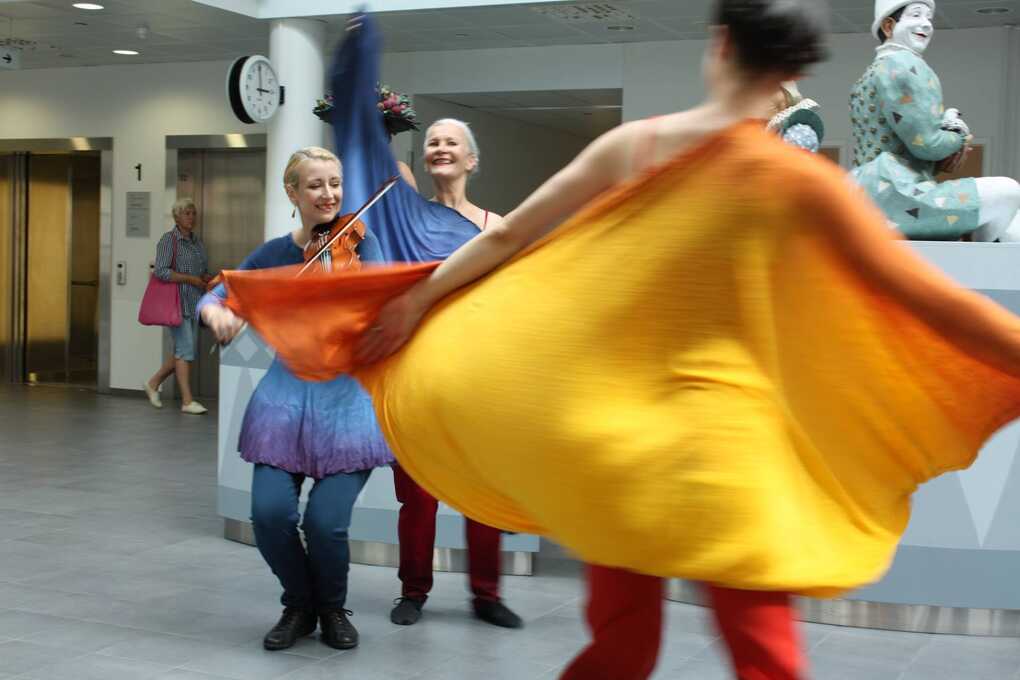 Two dancers and a violinist in colourful clothes performing in a hospital lobby