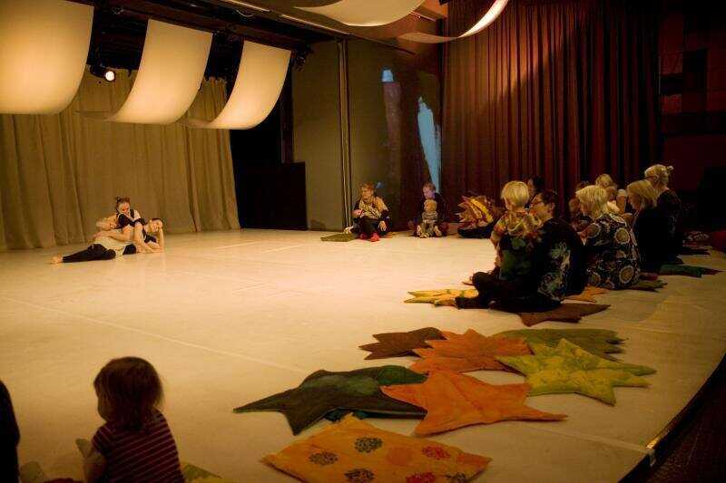 Three dancers leaning towards each other on the floor of the performance hall, with the viewers sitting on cushions on the floor