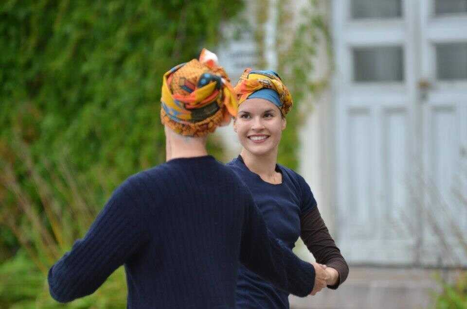 Naispari oransseissa päähineissä tanssii vastakkain pitäen toisistaan käsistä kiinni.