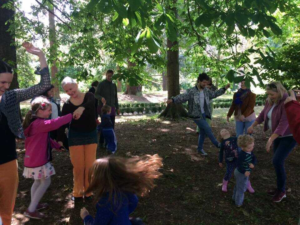 Aikuisia ja lapsia tanssii vihreän metsän siimeksessä.